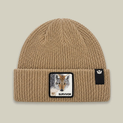 The Survivor Beanie by Goorin Bros is a beige ribbed knit beanie with a wolf head patch featuring embroidery and the word "Survivor" on the front, displayed against a neutral background.