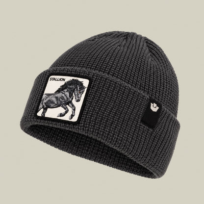 The Stallion Beanie by Goorin Bros is a charcoal gray ribbed knit beanie featuring a white patch with a black stallion illustration and text on the front, displayed against a neutral background.