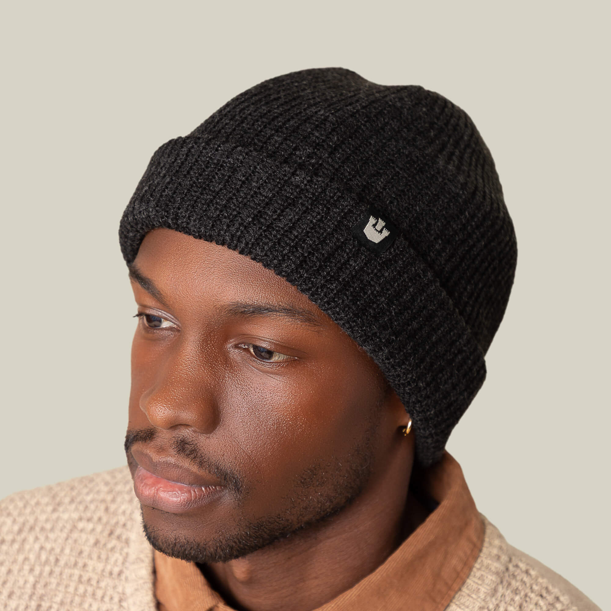 A person wearing the Goorin Bros. Air to Fakie black beanie with a small logo, paired with a beige textured jacket over a brown collared shirt, stands against a plain background. The lightweight poly knit offers all-season comfort and style.