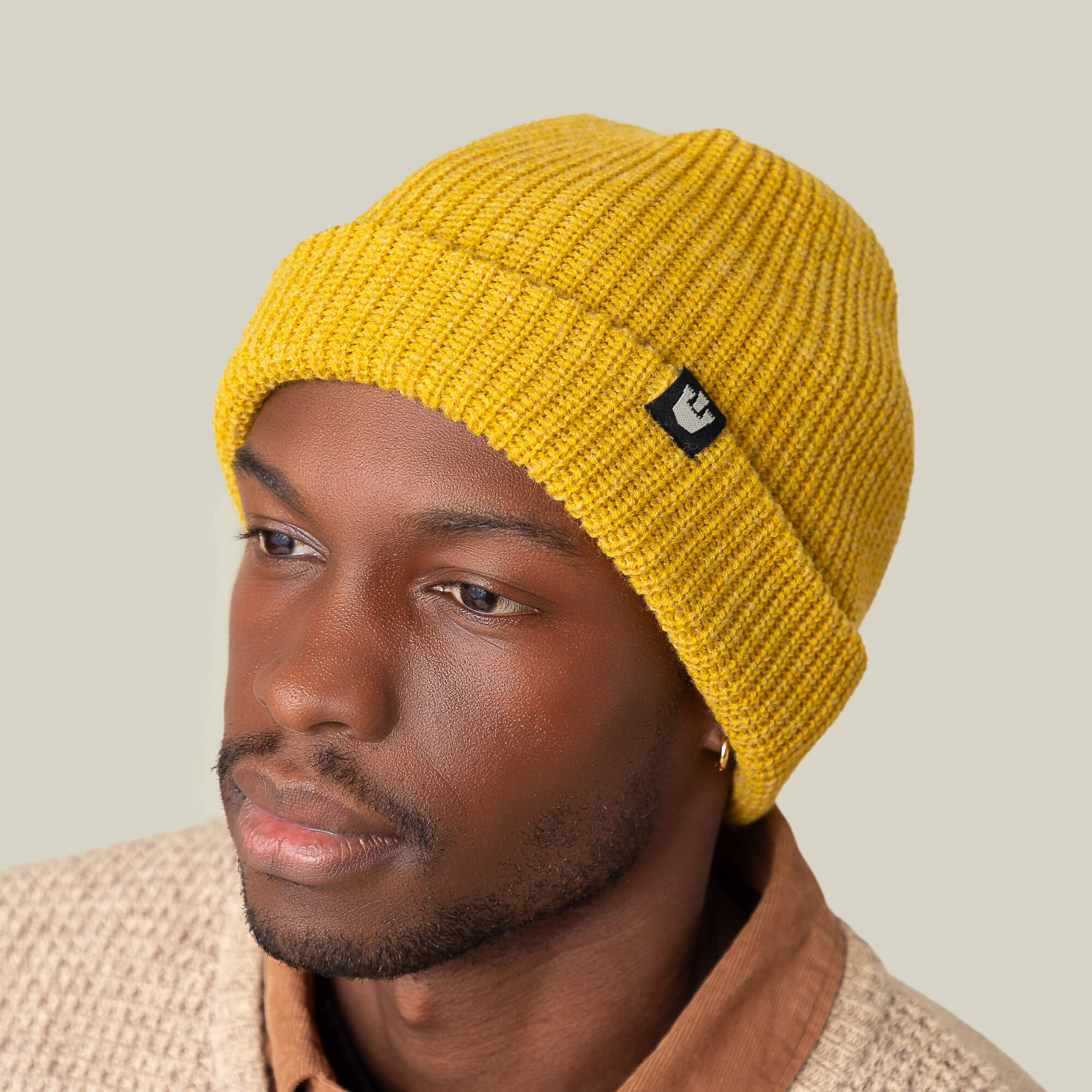 A man in a yellow Goorin Bros. Air to Fakie all-season Watchman beanie, brown collared shirt, and beige textured jacket poses against a plain light background.