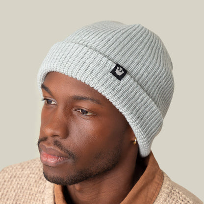 A man wears the Goorin Bros. Air to Fakie light gray beanie in lightweight poly knit and a textured beige sweater, glancing to the side against a plain background, highlighting versatile all-season style.