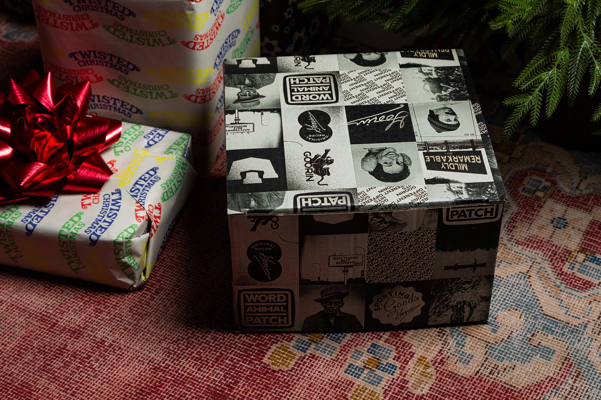 A square Goorin Gift Box by Goorin Bros., wrapped in black-and-white collage paper, sits on a patterned rug next to another present with a red bow—an ideal surprise for any headwear enthusiast.