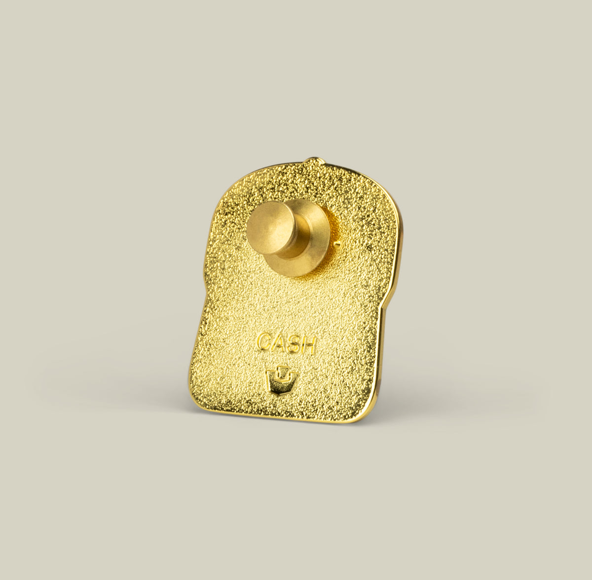 The Goorin Bros. Cash Cow Trucker Pin is a gold-colored zinc alloy bread slice with a textured finish, button backing, and “CASH” engraved on it.