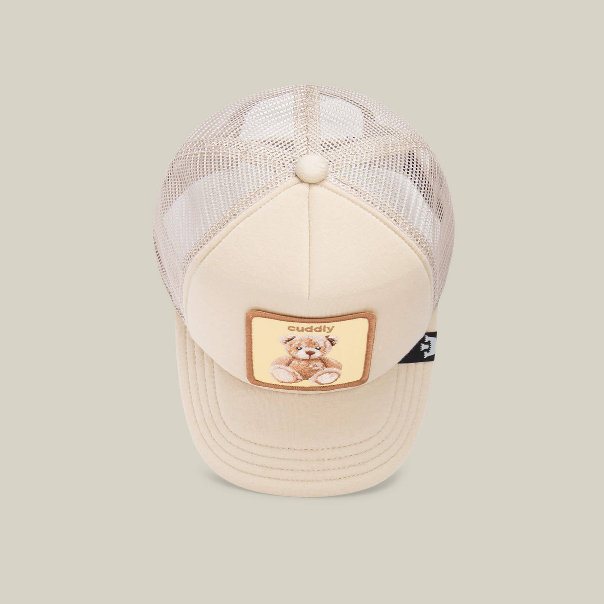 The Goorin Bros. "Cuddle Time" kids trucker cap features beige mesh and a patch with a teddy bear and "cuddly" on the front—perfect for cozy hat lovers.