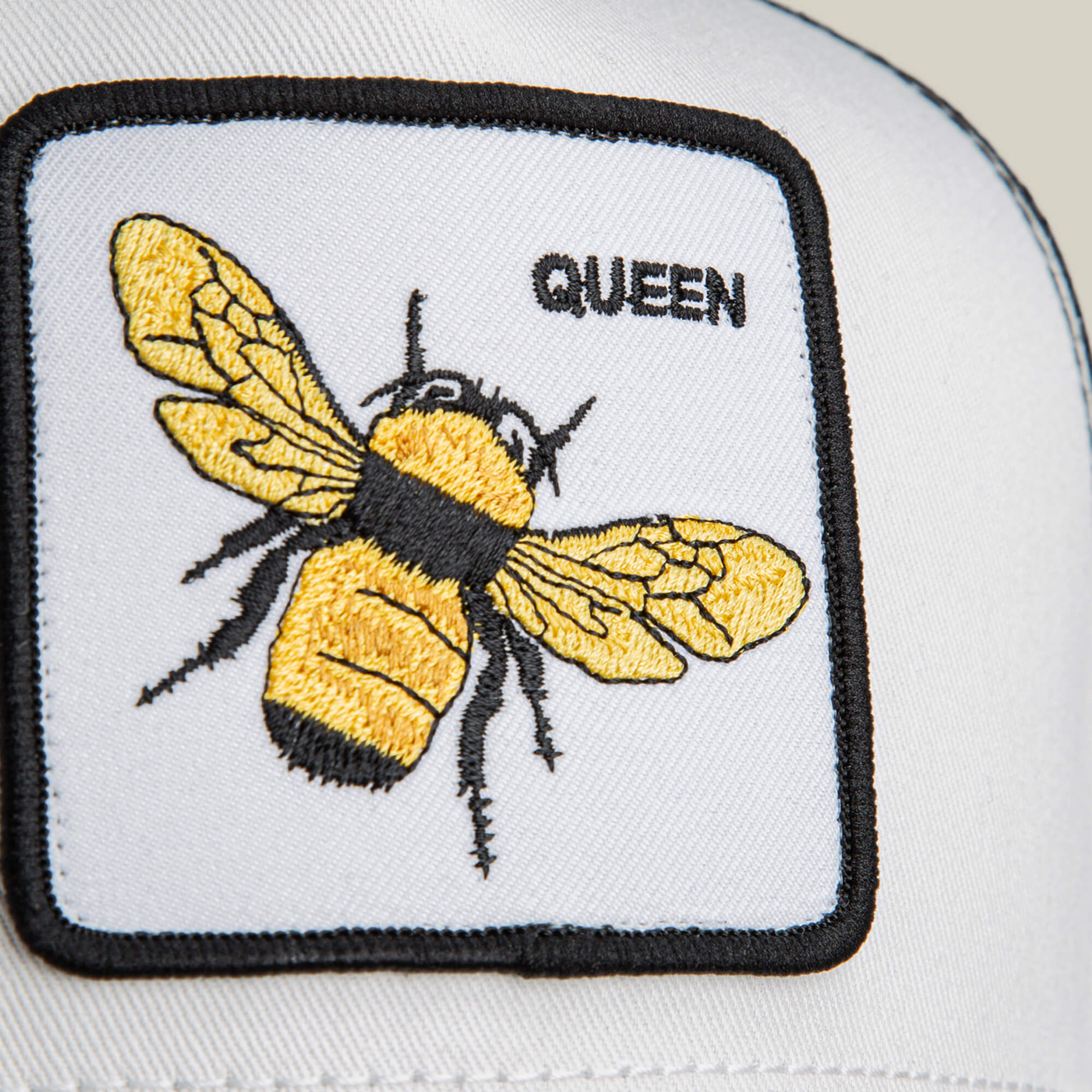 Close-up of The Queen Bee Mini kids cap by Goorin Bros., featuring a golden bee patch and "QUEEN" stitched in black with yellow and black embroidered details.