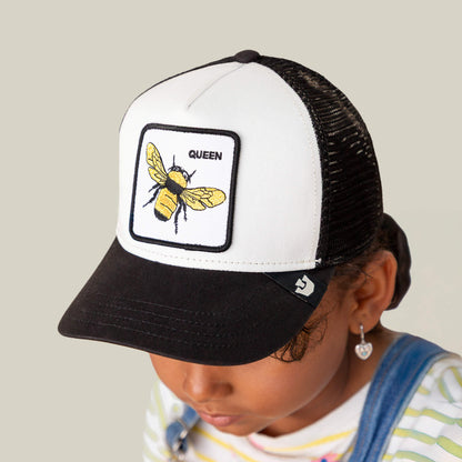 A child wears The Queen Bee Mini kids cap by Goorin Bros., a black and white hat with a golden bee patch labeled QUEEN on the front.