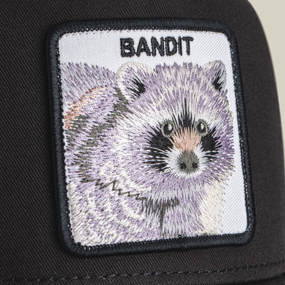 The Goorin Bros. Bandit Trucker Mini is a black trucker hat with an embroidered white patch featuring a detailed raccoon face and the word "Bandit" in black text.