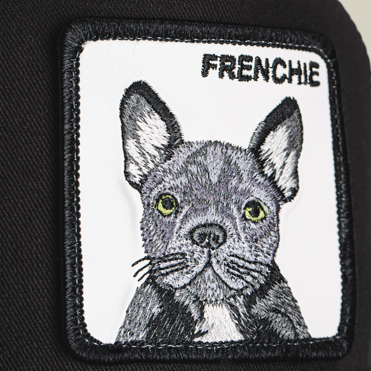 The Goorin Bros. Frenchie Trucker Mini is a black and white trucker hat featuring an embroidered French bulldog patch with yellow-green eyes on the front panel.