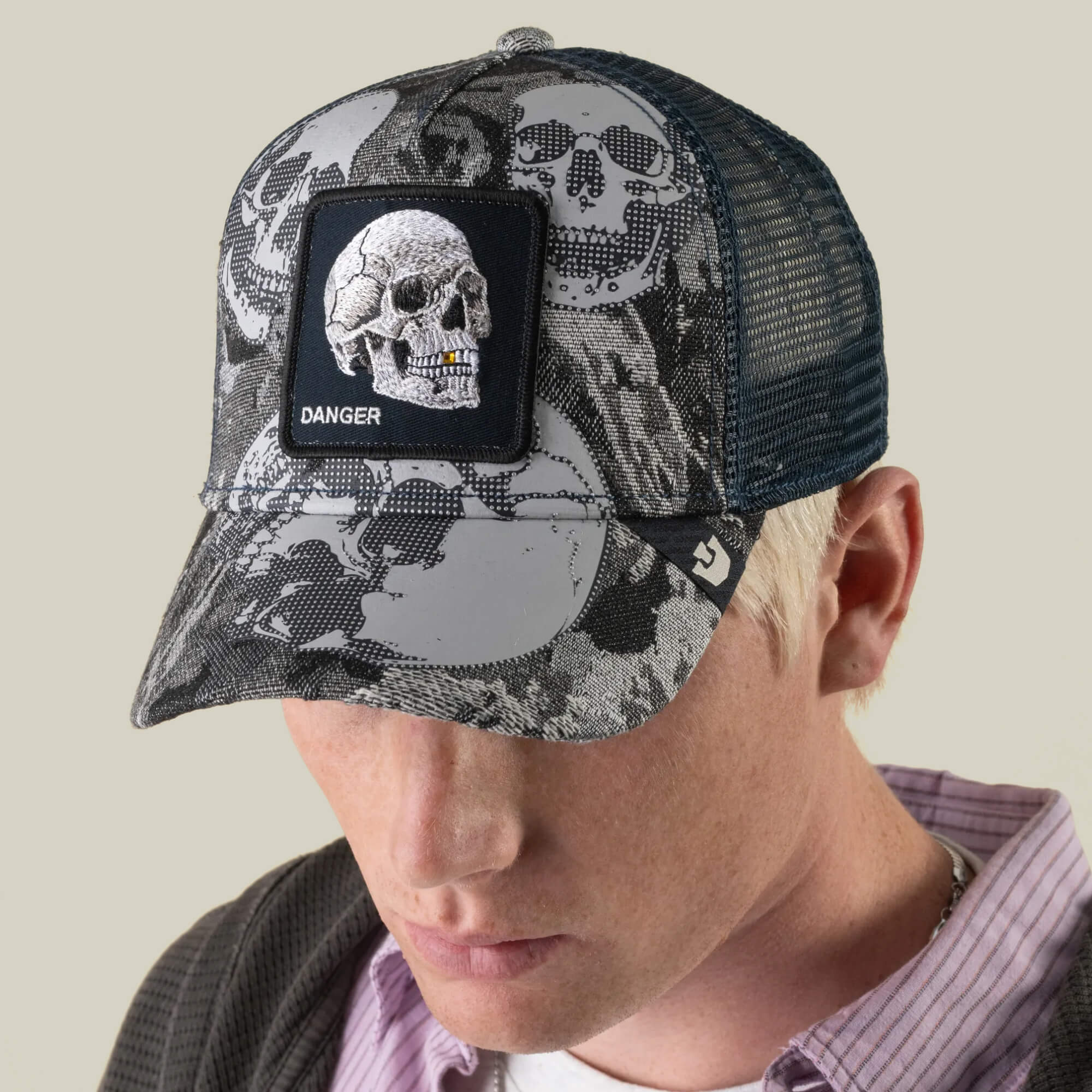 A person wearing the Goorin Bros. “Bone Head Danger” mesh-back trucker cap, featuring an embroidered skull patch and the word DANGER on the front, looks downward.