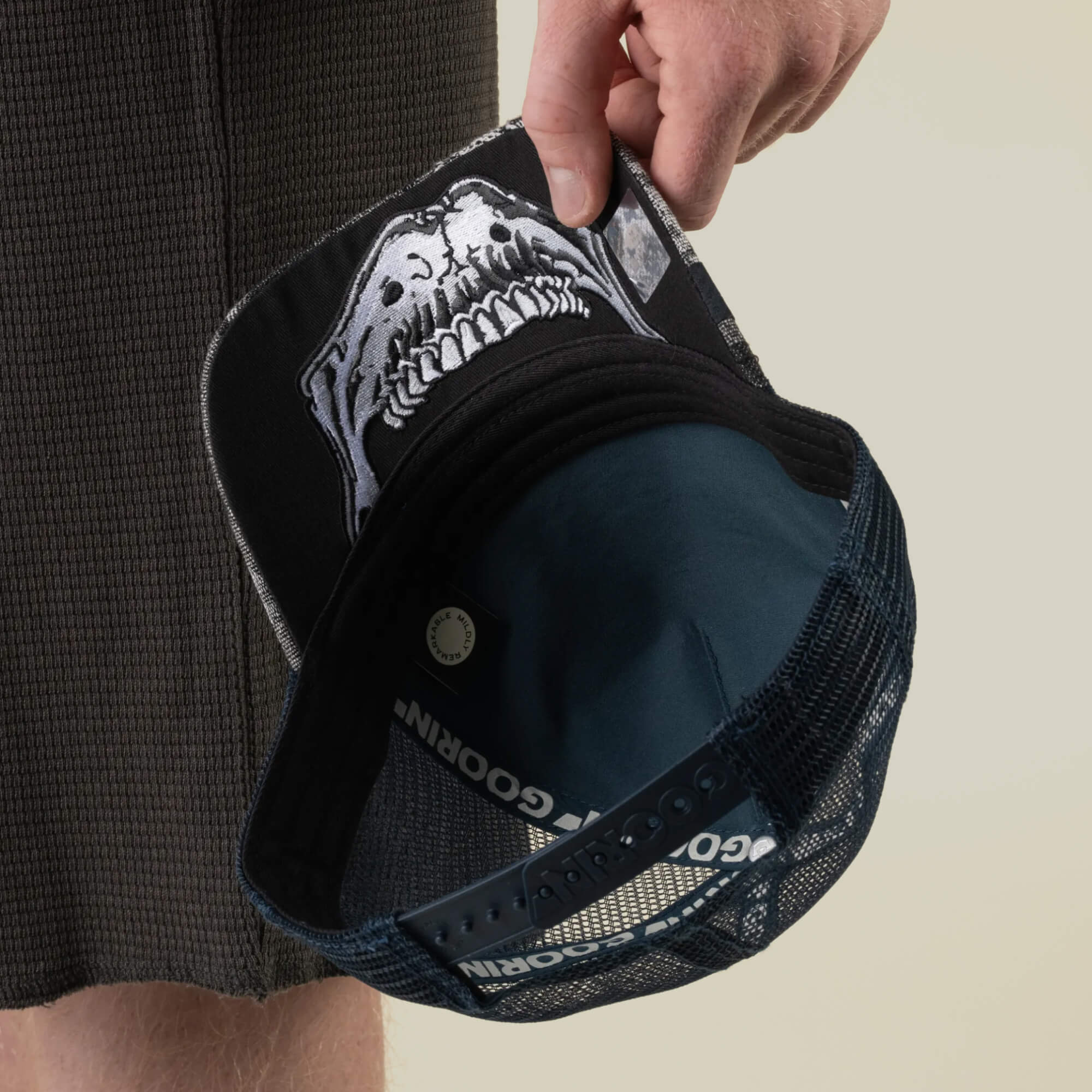 A person holds the Goorin Bros. Bone Head Danger black mesh-back trucker hat, featuring a striking white animal skull graphic printed on the underside of the brim.
