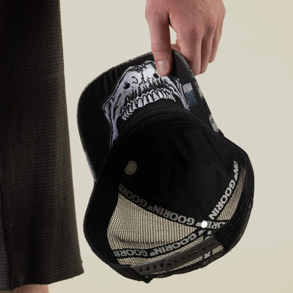 A person holds the Bone Head Unalive trucker hat by Goorin Bros., featuring a black and white skull design, a breathable mesh back, and distinctive Goorin Bros. branding inside.