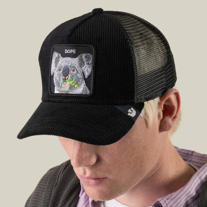 A man wearing the Goorin Bros. Corduroy Dope hat, which features a black mesh back and an embroidered patch of a koala eating leaves with the word “DOPE” above it.