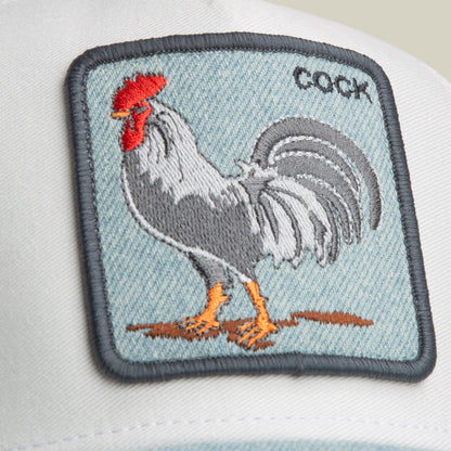 Introducing the Denim Rooster by Goorin Bros.—a white baseball cap featuring a fabric patch with an embroidered rooster and the word “COCK” in the upper right corner. Designed in a classic trucker hat style, this playful yet timeless accessory brings distinctive charm to any collection.