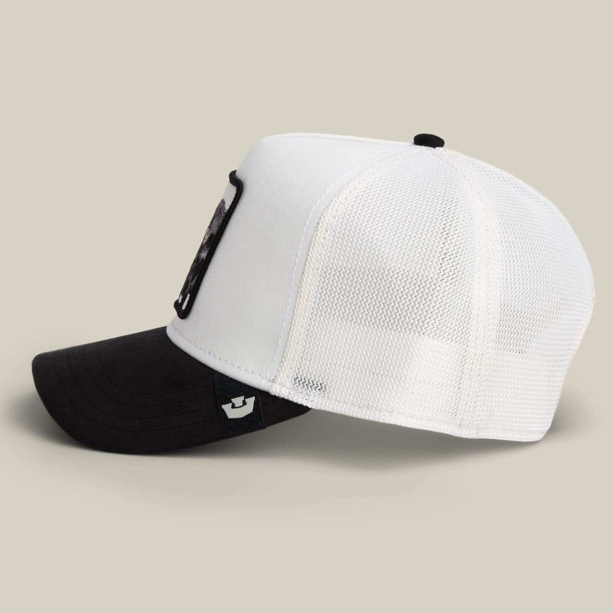 The Goorin Bros. Suede Ruthless hat is a black and white trucker cap with a white mesh back, a black bill, and a bold black patch on the front, displayed from a side angle against a neutral background.