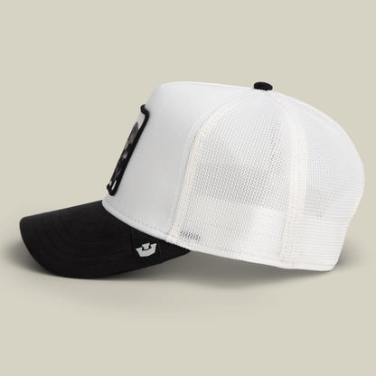 The Goorin Bros. Suede Ruthless hat is a black and white trucker cap with a white mesh back, a black bill, and a bold black patch on the front, displayed from a side angle against a neutral background.