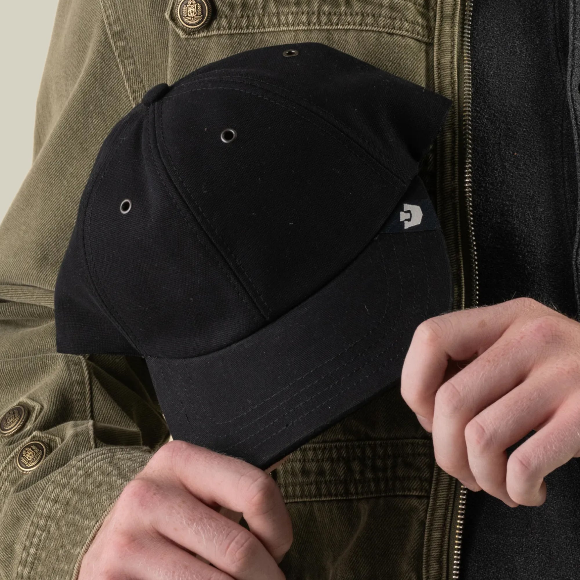 A person in a green jacket holds the Goorin Bros. “Mineral Road” mixed-material black baseball cap with both hands.