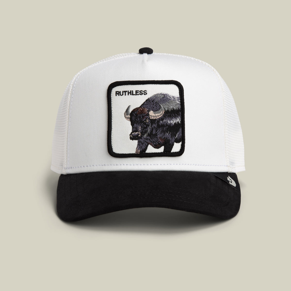The Goorin Bros. Suede Ruthless is a white and black trucker hat featuring a patch with a buffalo and “RUTHLESS” embroidered above the animal, displayed against a plain light background. This bold trucker hat combines classic style with striking embroidery for an unmistakable look.