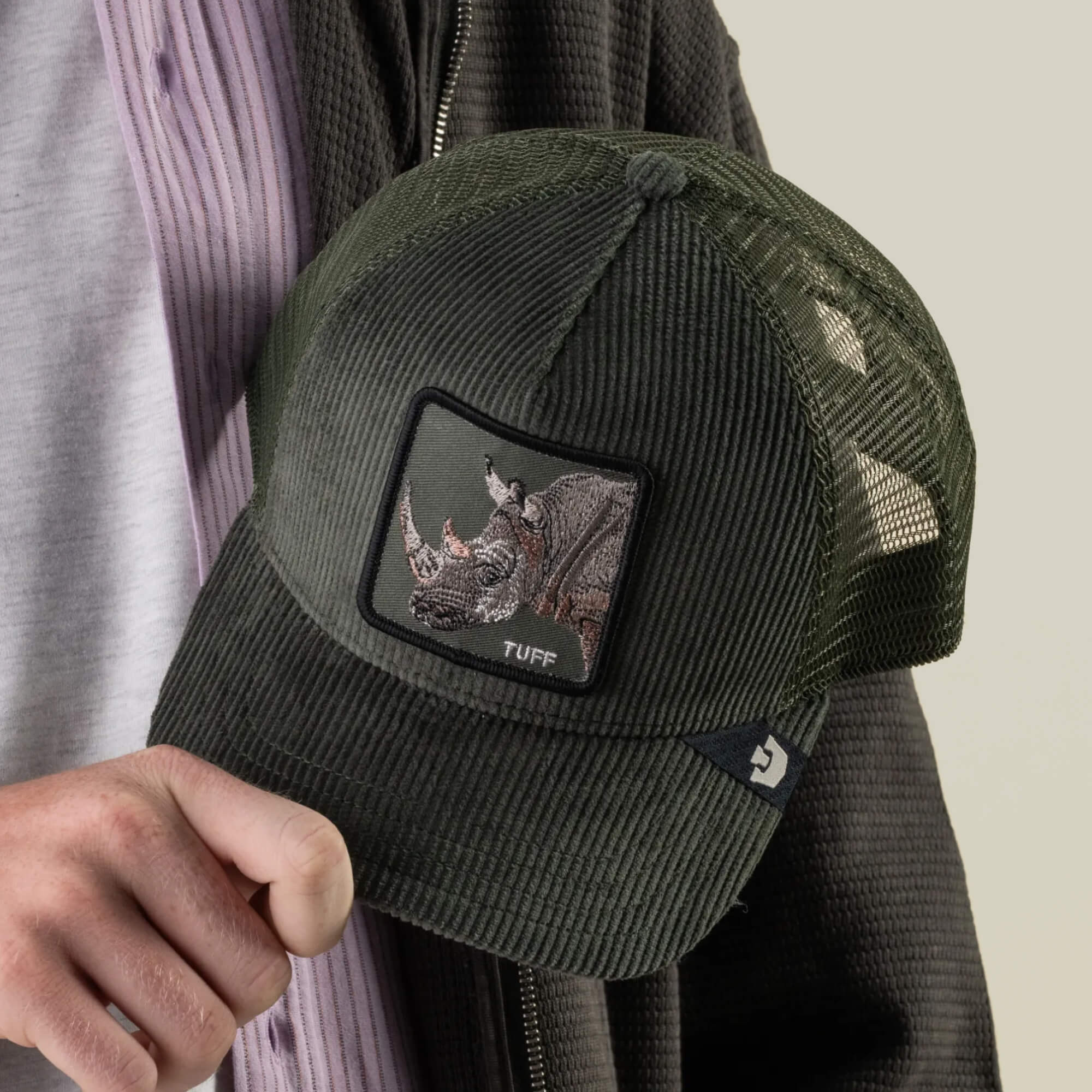 A person holds the Goorin Bros. Corduroy Tuff hat, made from a sturdy polyester-cotton blend in green corduroy, featuring a mesh back and an embroidered rhino patch with “TUFF” stitched beneath it.
