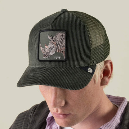 A person wearing the Goorin Bros. Corduroy Tuff hat—a dark green trucker hat crafted from a durable polyester-cotton corduroy blend, featuring a rhino embroidered patch with the word “TUFF”—looks downward against a plain background.