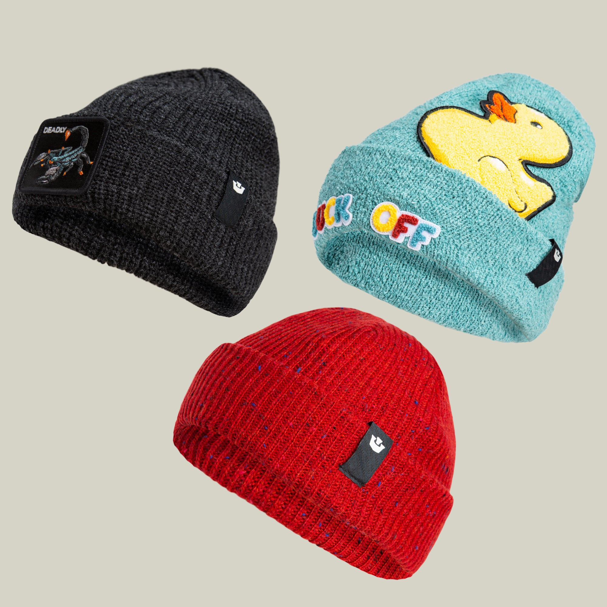 The Beanie Bundle by Goorin Bros. includes three warm beanies: one dark gray with a patch, one light blue featuring a yellow duck and multicolored lettering, and one solid red, each adorned with a small black tag.