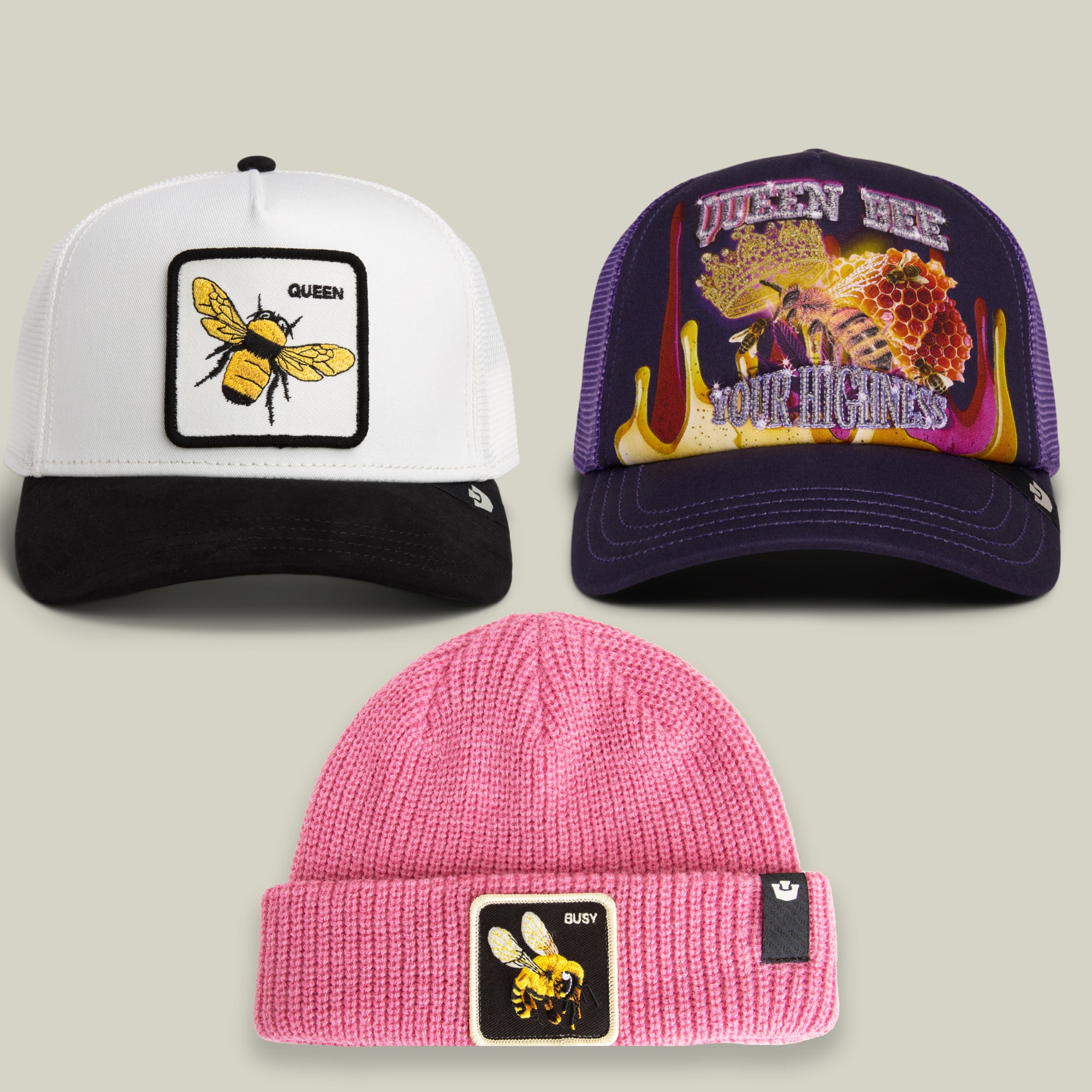 The Bee’s Knees Bundle from Goorin Bros. includes three vibrant, concert-poster-inspired hats: a black and white trucker hat with a bee patch, a purple cap featuring Queen Bee graphics, and a pink beanie adorned with a bee patch and the word “Busy”—each boasting bold details and colorful design elements.