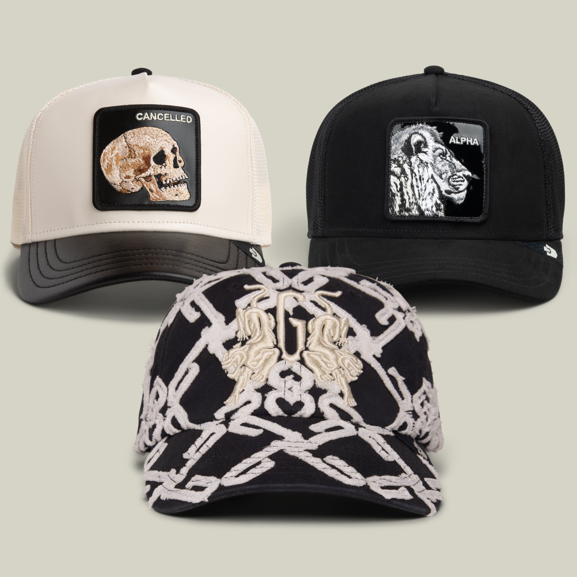 The Goorin Bros. Black and White and Rad All Over Bundle includes three caps: a cream cap with a skull patch labeled “CANCELLED,” a black blackout trucker cap featuring a lion patch labeled “ALPHA,” and a black cap with a woven pattern and an embroidered crest on the front.