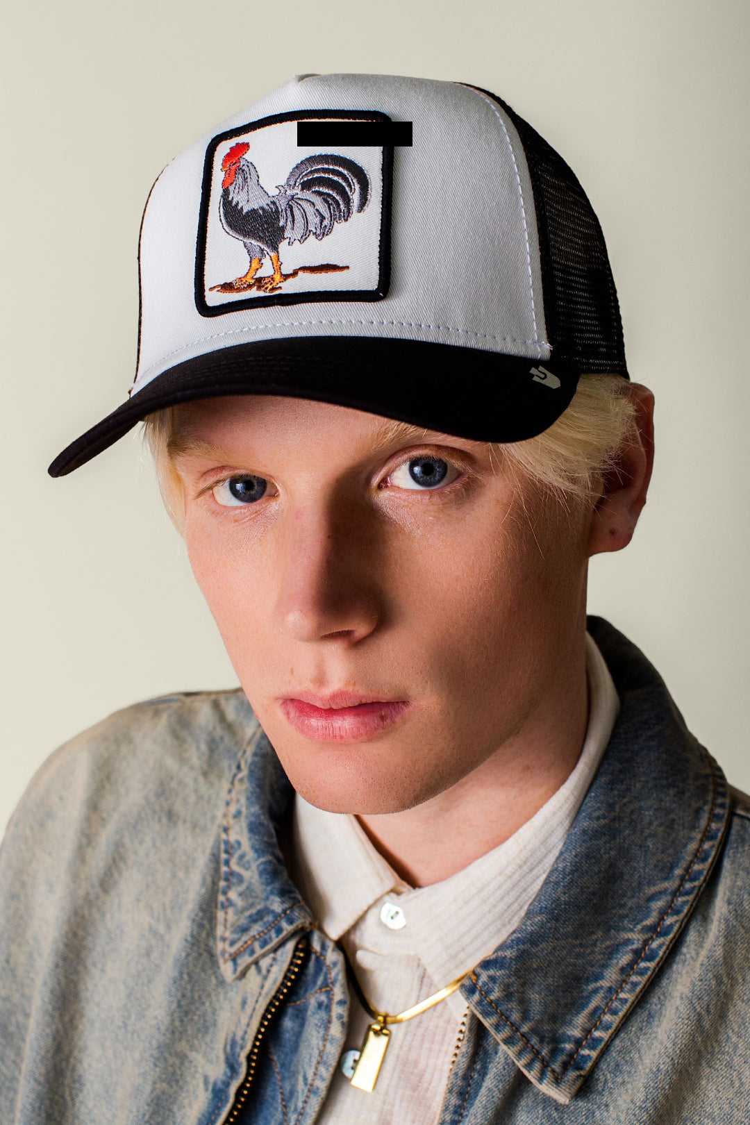Person wearing a cap with a rooster patch against a plain background