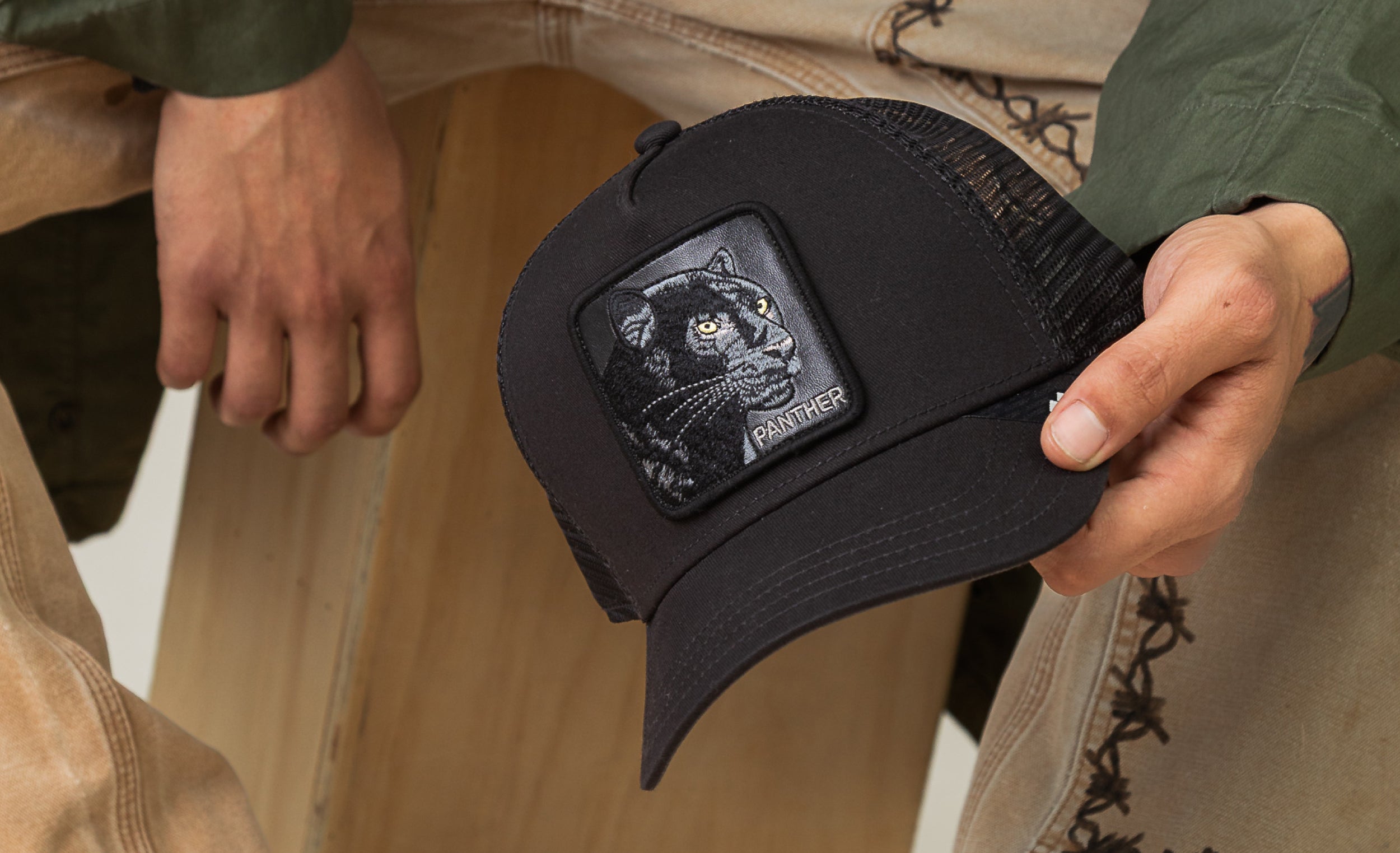 A person holding a black Goorin trucker hat with a patch featuring an embroidered panther, showcasing the brand’s reputation for durable hats.