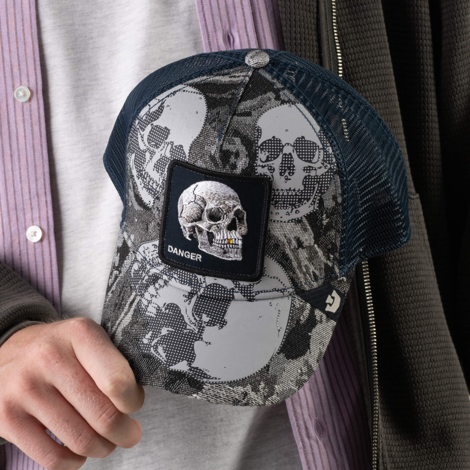 A person holds the Goorin Bros. Bone Head Danger cap, featuring a striking skull print and a patch embroidered with a skull and the word “DANGER.”.