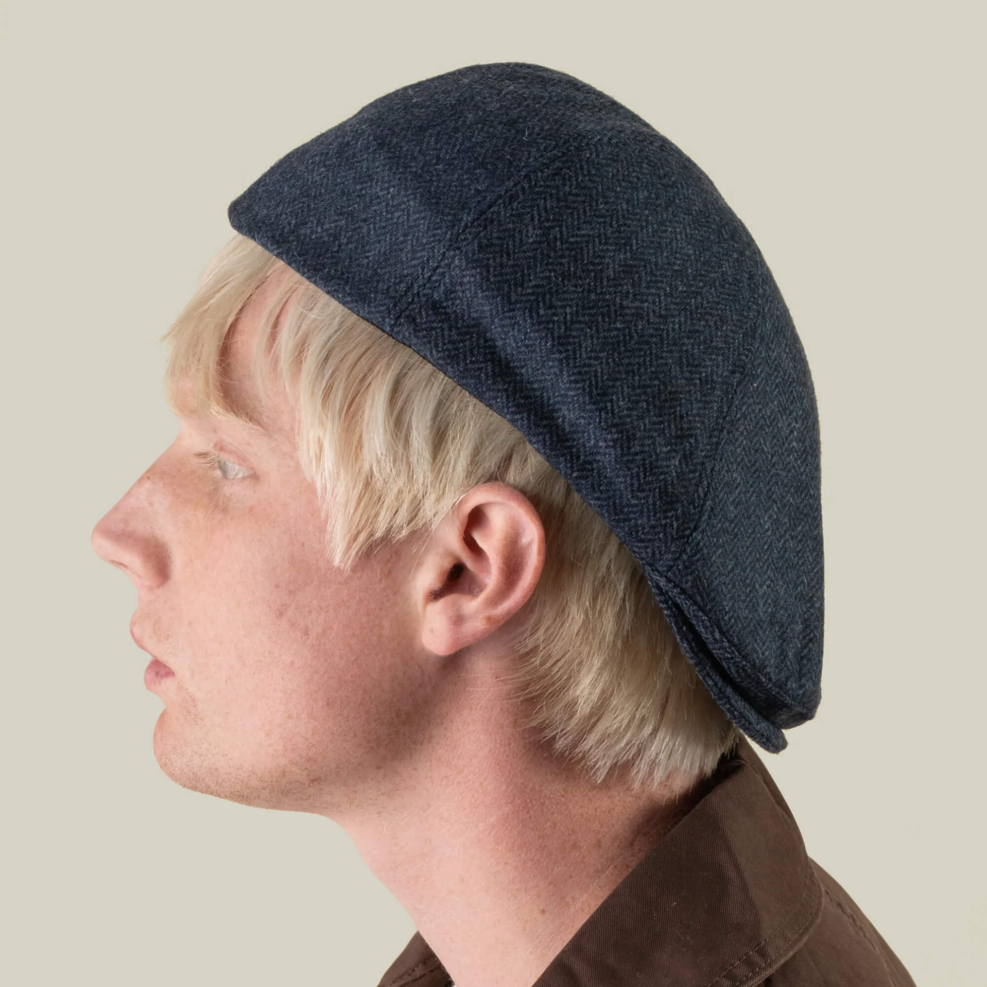A person with blond hair is shown in profile against a plain background, wearing the “Harry Bones” dark blue flat cap by Goorin Bros., made in the USA.