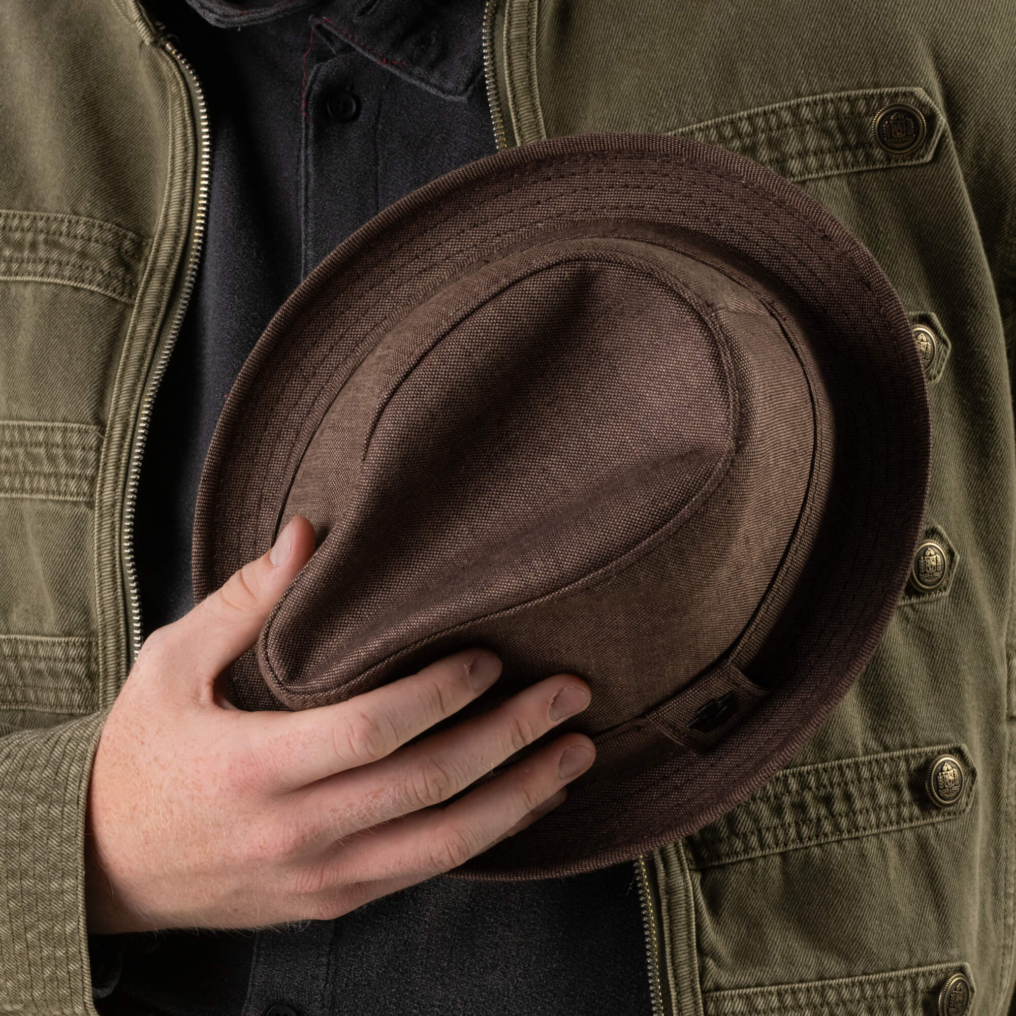 A person wearing a green jacket holds the Goorin Bros. Charlie Pants in front of their chest with one hand.