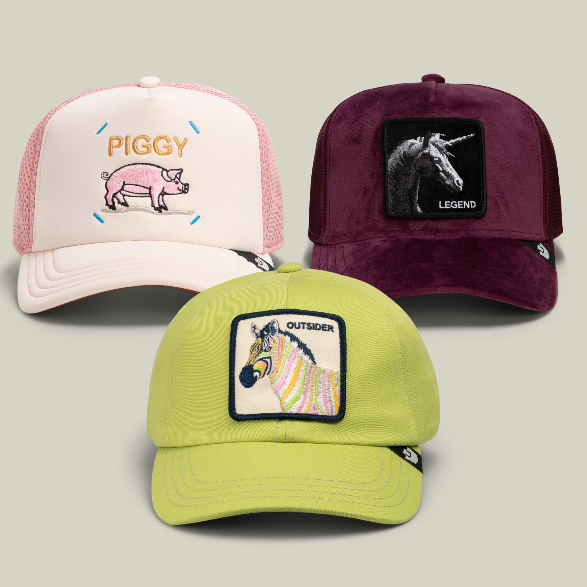 The Goorin Bros. Color Lover Bundle includes three baseball caps: one in pastel pink featuring a pig and the word “PIGGY,” one in deep wine adorned with a unicorn and “LEGEND,” and one in chartreuse green showcasing a zebra and the word “OUTSIDER” on the front panels.