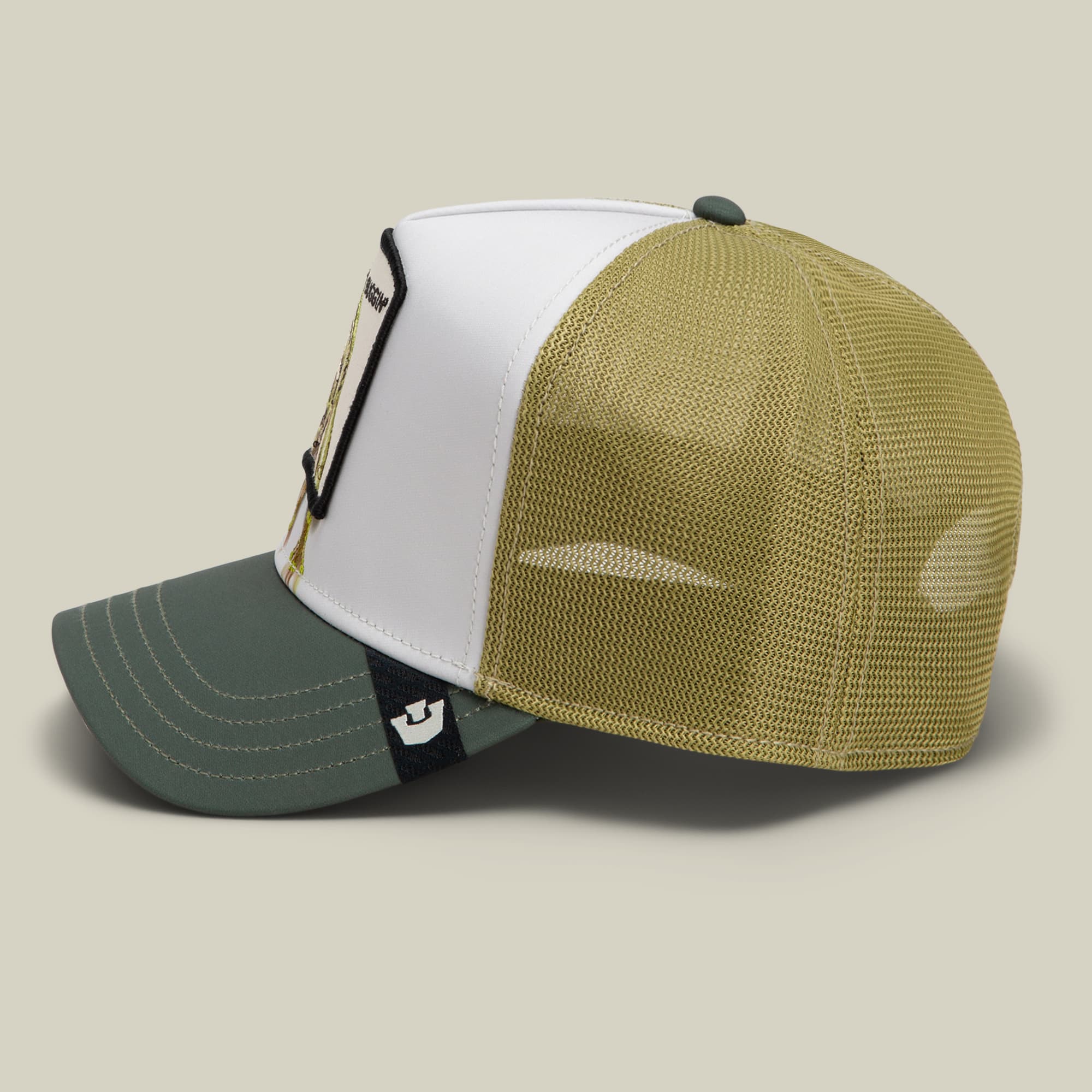 The Goorin Bros. Migration - Buggin trucker hat features a color-block design with a white front panel, khaki mesh back, and sage green bill, showcasing a small embroidered patch on the front.